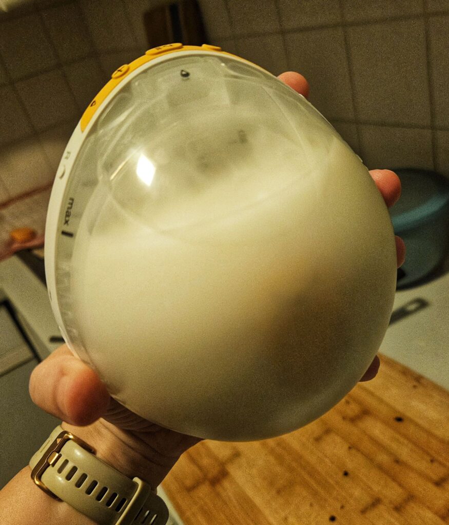 Hand hält eine gefüllte Medela Magic Inbra mit Fokus auf der Vorderseite der Milchpumpe.