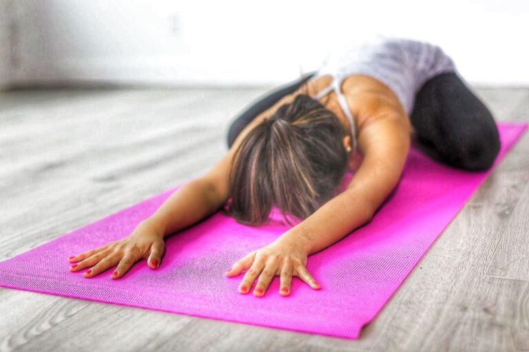 Frau in der Child’s Pose während einer sanften Yogastunde nach der Geburt.