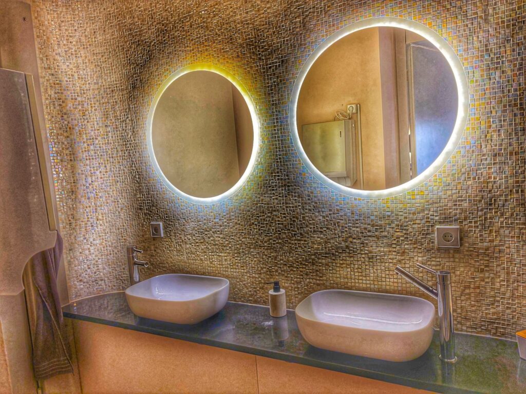 Badezimmer im Spirit Yoga Charlottenburg mit gefliester Wand, zwei runden Spiegeln über ovalen Waschbecken