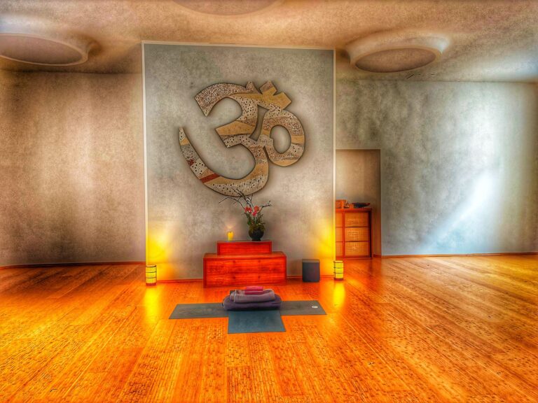 Großer Yogaraum im Spirit Yoga Charlottenburg, Bereich der Yogalehrerin mit Blume, kleinen Lampen, Lautsprechern und gekreuzten Yogamatten mit Zubehör