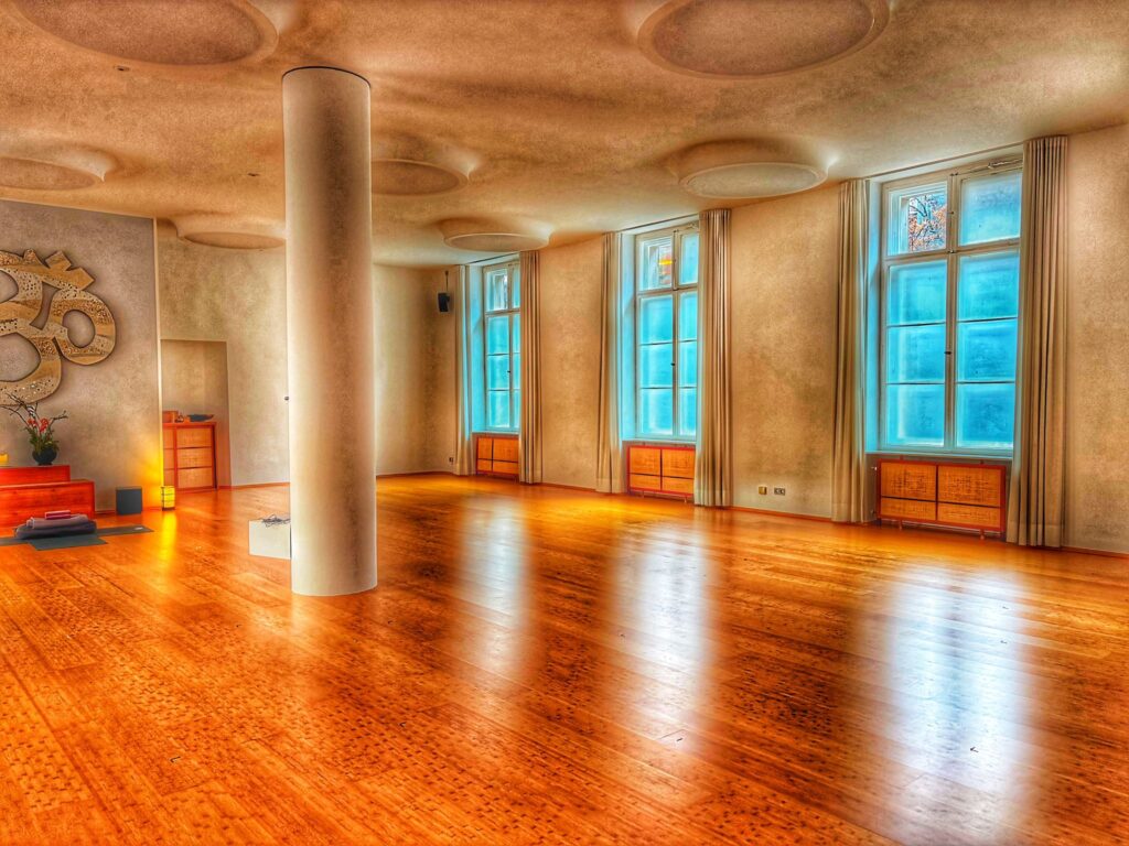 Großer Yogaraum im Spirit Yoga Charlottenburg mit Holzboden, großen Fenstern, zentraler Säule und runden Deckenlampen