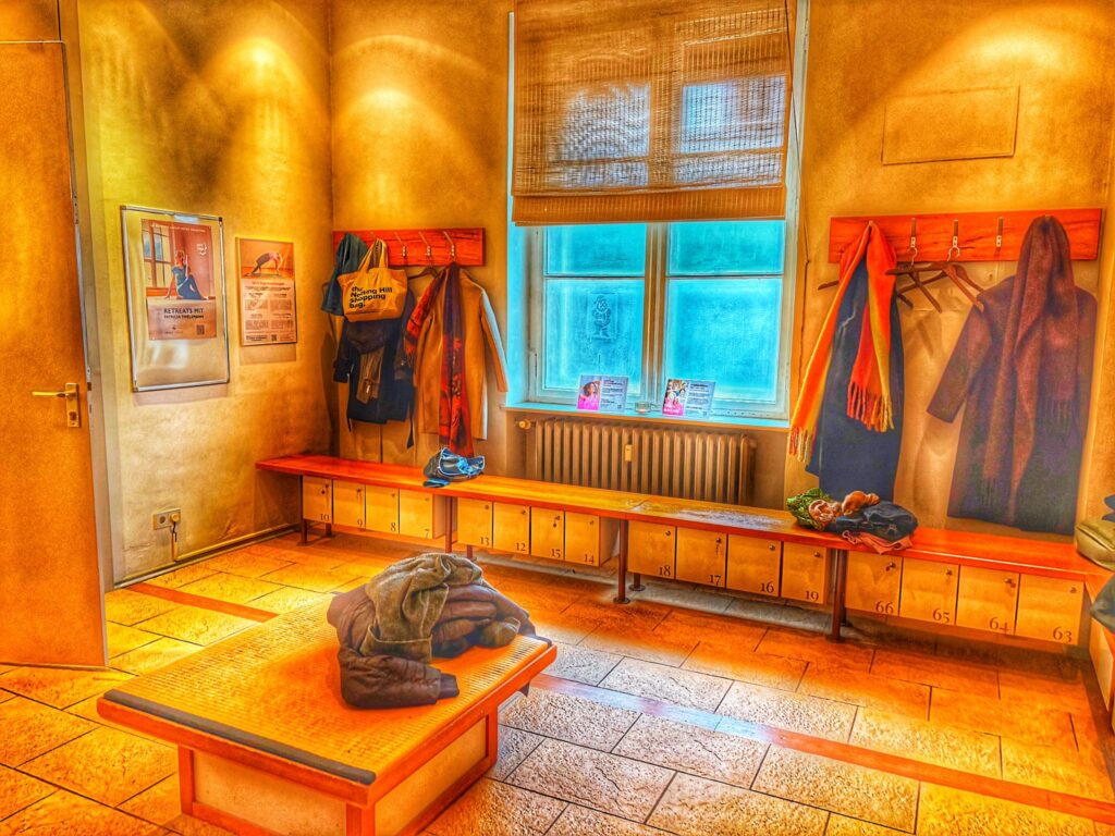 Umkleidebereich im Spirit Yoga Charlottenburg mit Fliesenboden, Bänken an den Seiten und zentraler Bank, Jacken hängen an den Haken